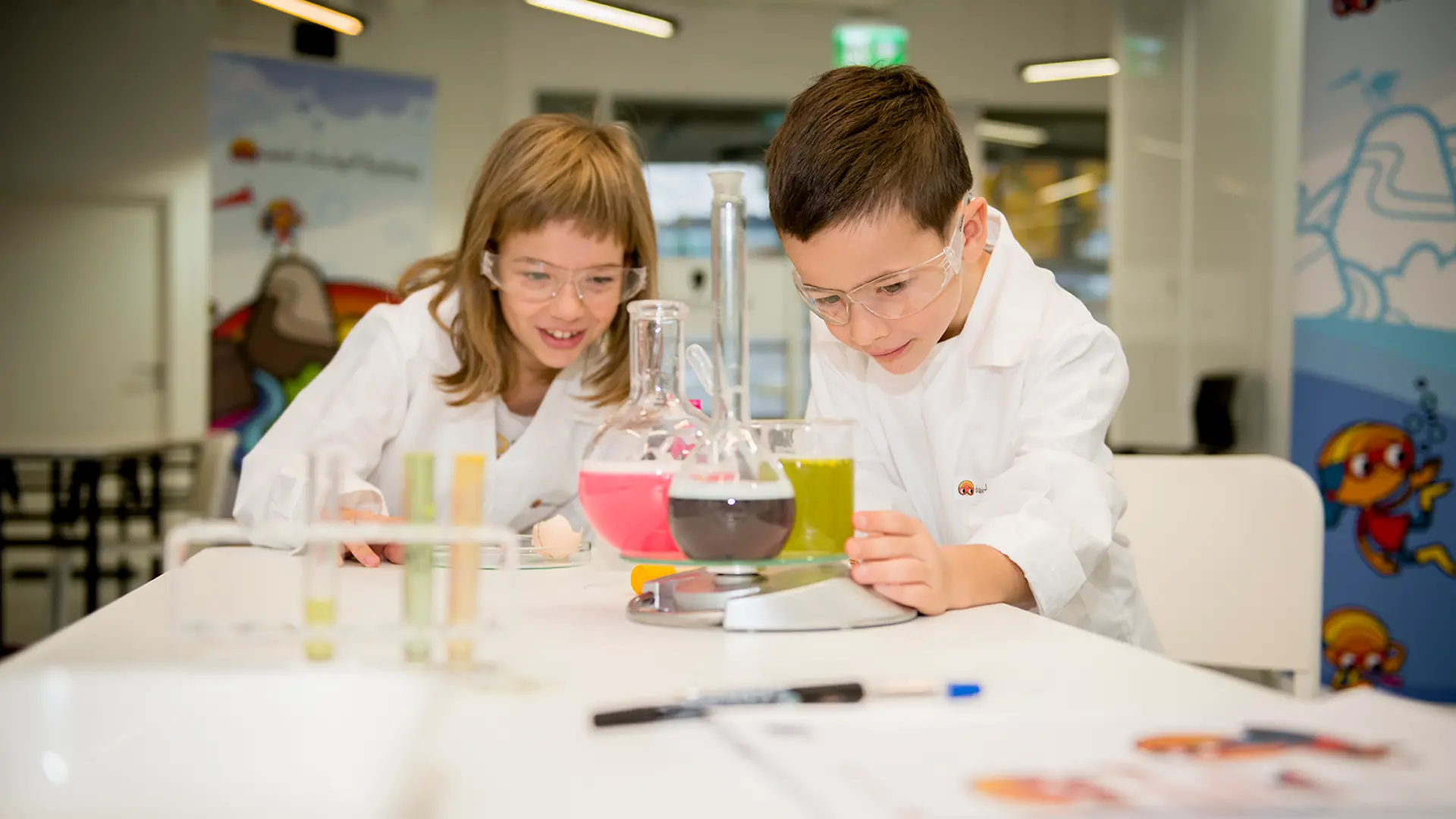 boy and girl in lab coat looking at a beaker