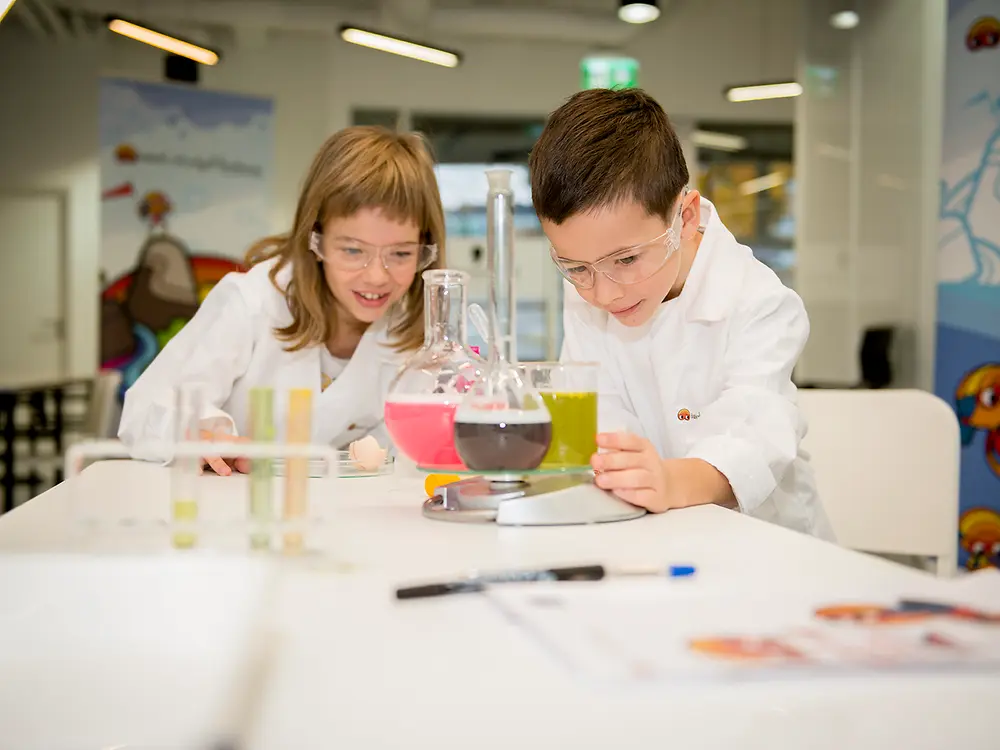 boy and girl in lab coat looking at a beaker