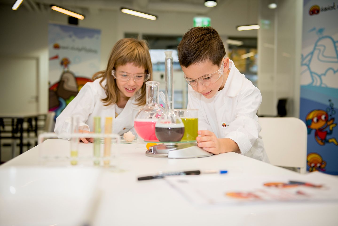 boy and girl in lab coat looking at a beaker