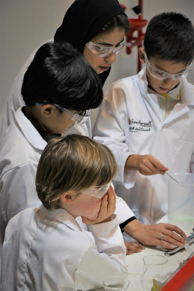 three children in lab coats with female teacher
