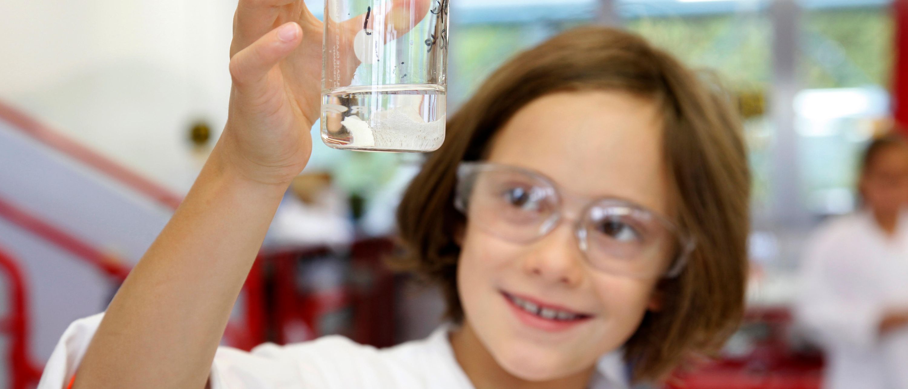 girl in lab coat looks at liquid in beaker