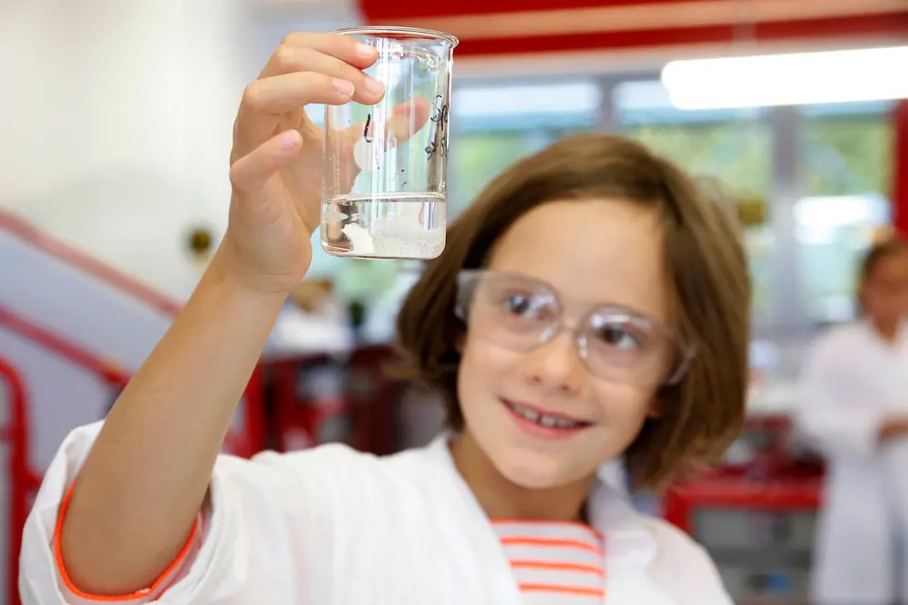 chica en bata de laboratorio mira líquido en vaso de precipitados