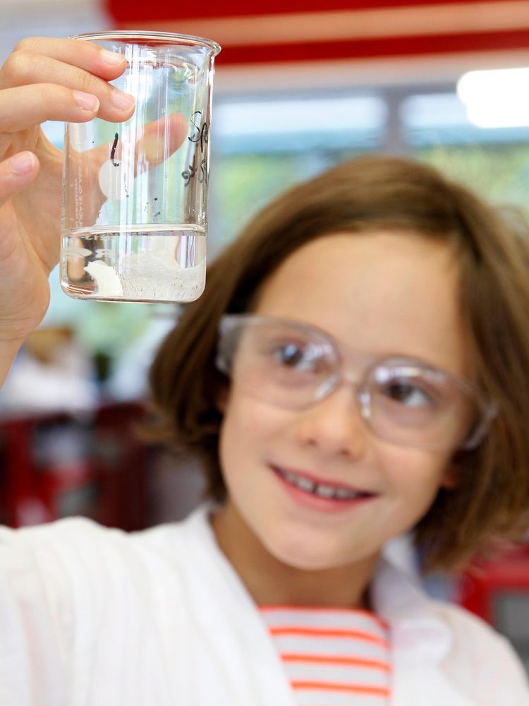 girl in lab coat looks at liquid in beaker