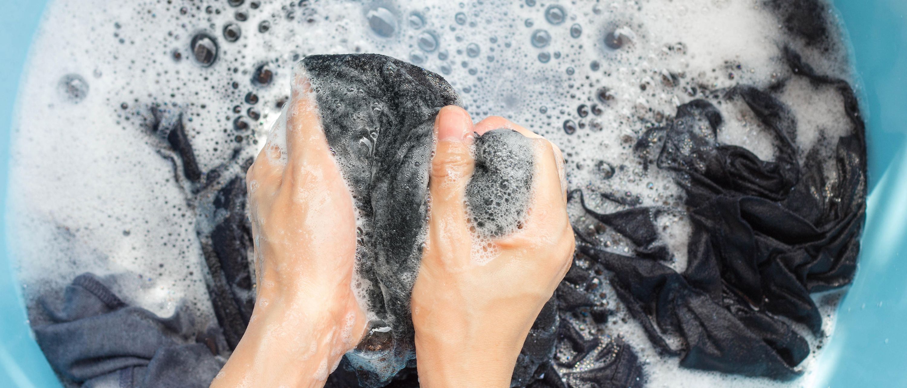 hands washing fabric in plastic bowl