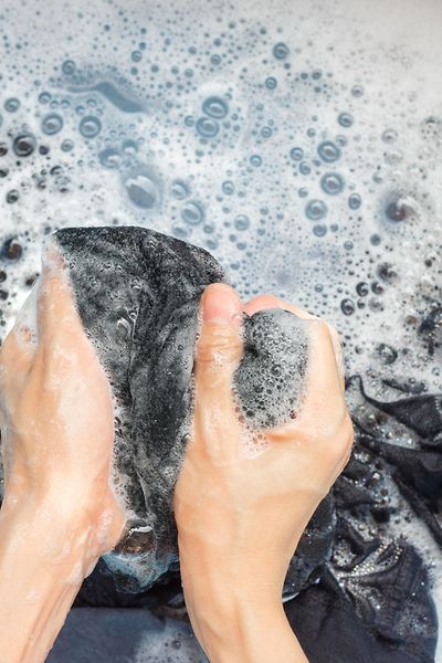 Nahaufnahme von Händen, die blaues Textil in einer Schüssel waschen