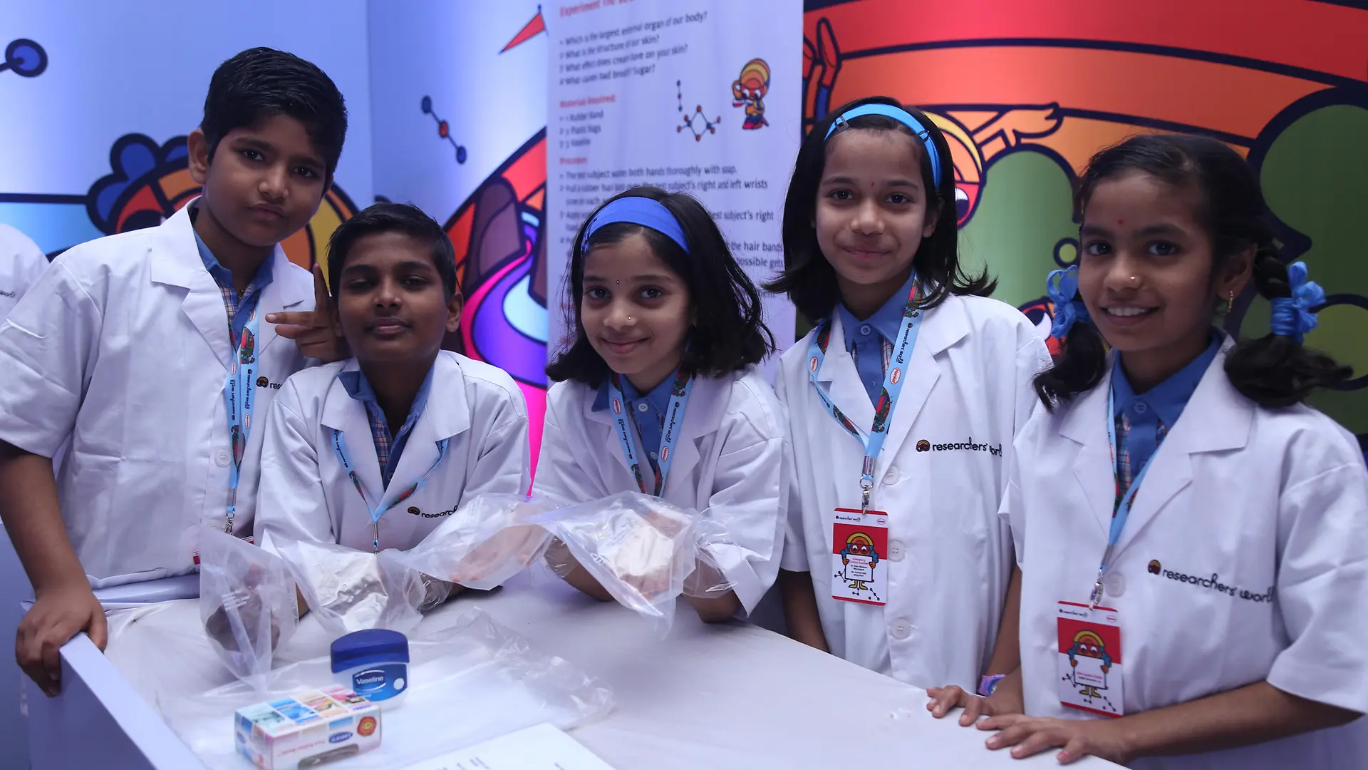 grupo de niños indios en batas de laboratorio de pie en una mesa blanca