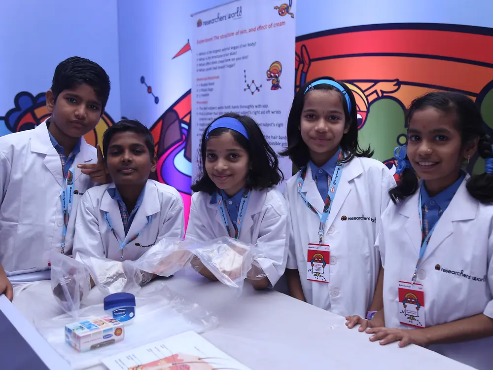 group of Indian children in lab coats standing at a white table