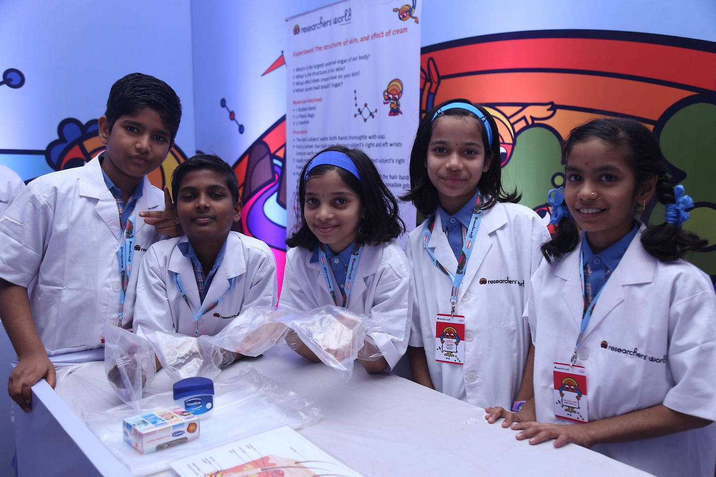grupo de niños indios en batas de laboratorio de pie en una mesa blanca