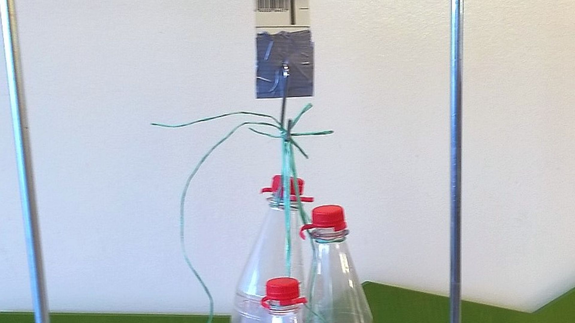 Tripod rod with paper loop hanging from it, from which hang bottles