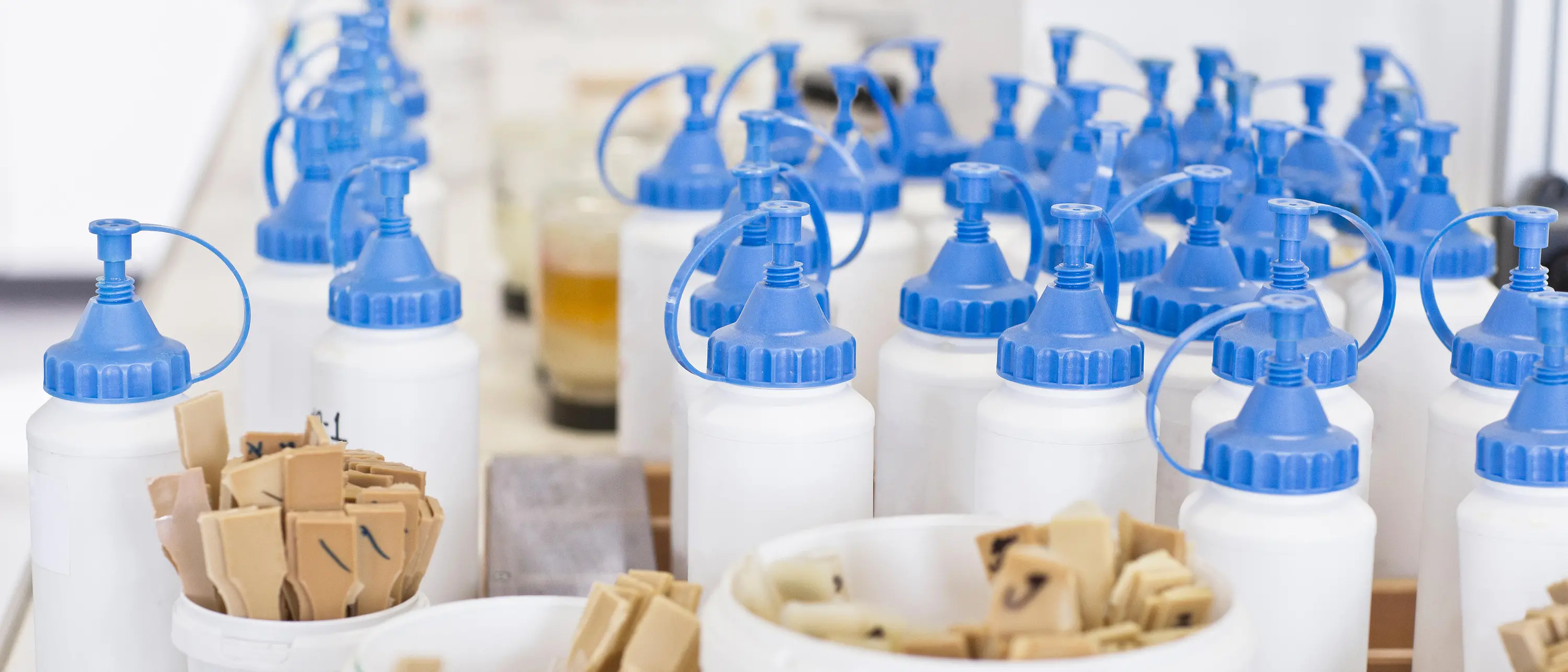 küçük tahta spatulalı bardakların altında mavi kapaklı beyaz plastik şişeler