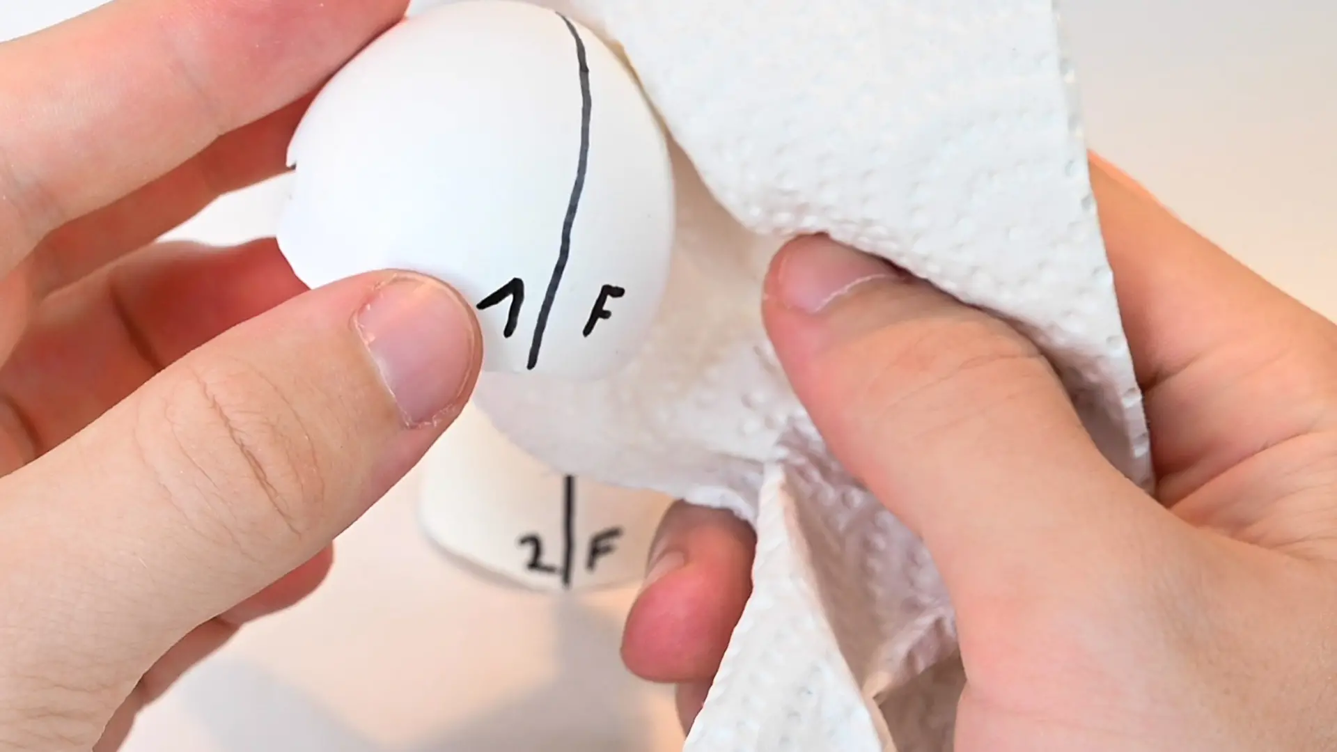 Nahaufnahme von Hand die mit Küchenpapier eine Eierschalhälfte abtupft