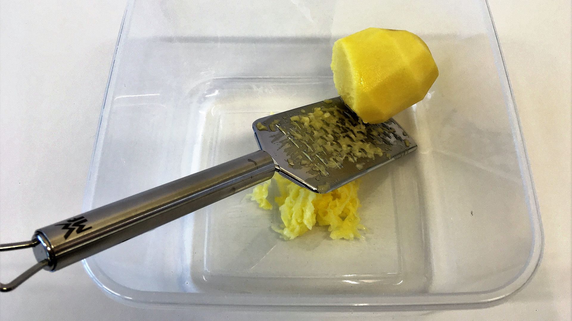 grater with pealed potato in plastic bowl