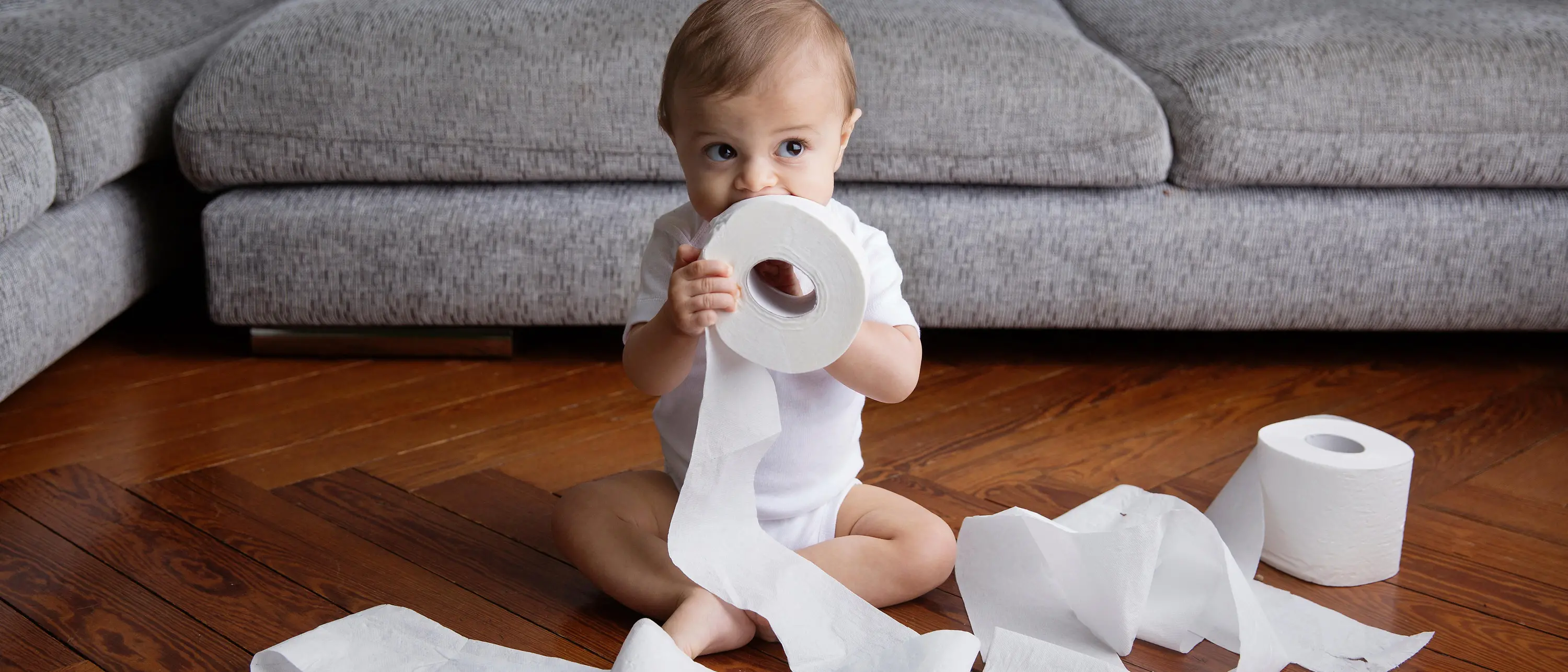 bebê sentado no chão com papel higiênico na frente do sofá