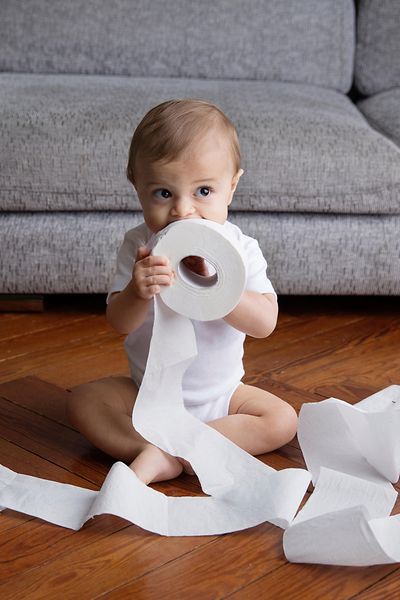 Baby mit zwei Rollen Toilettenpapier sitzt auf dem Boden
