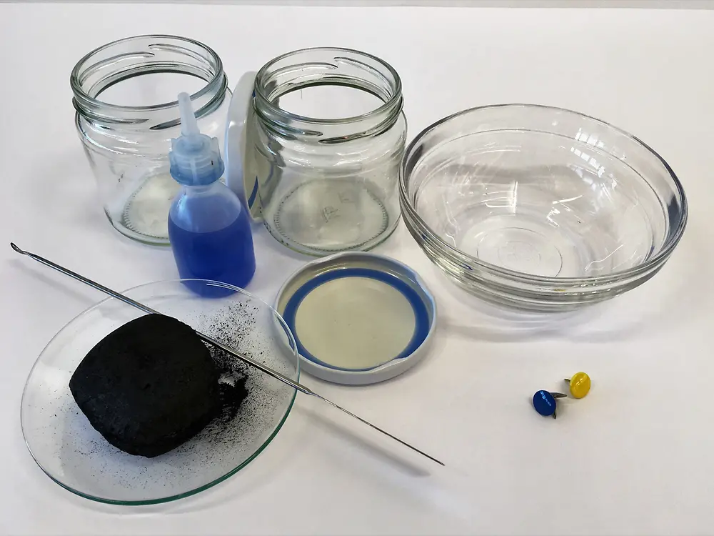 szklane słoiki i kokardę z kawałkiem węgla i małą plastikową butelką z niebieskim płynem