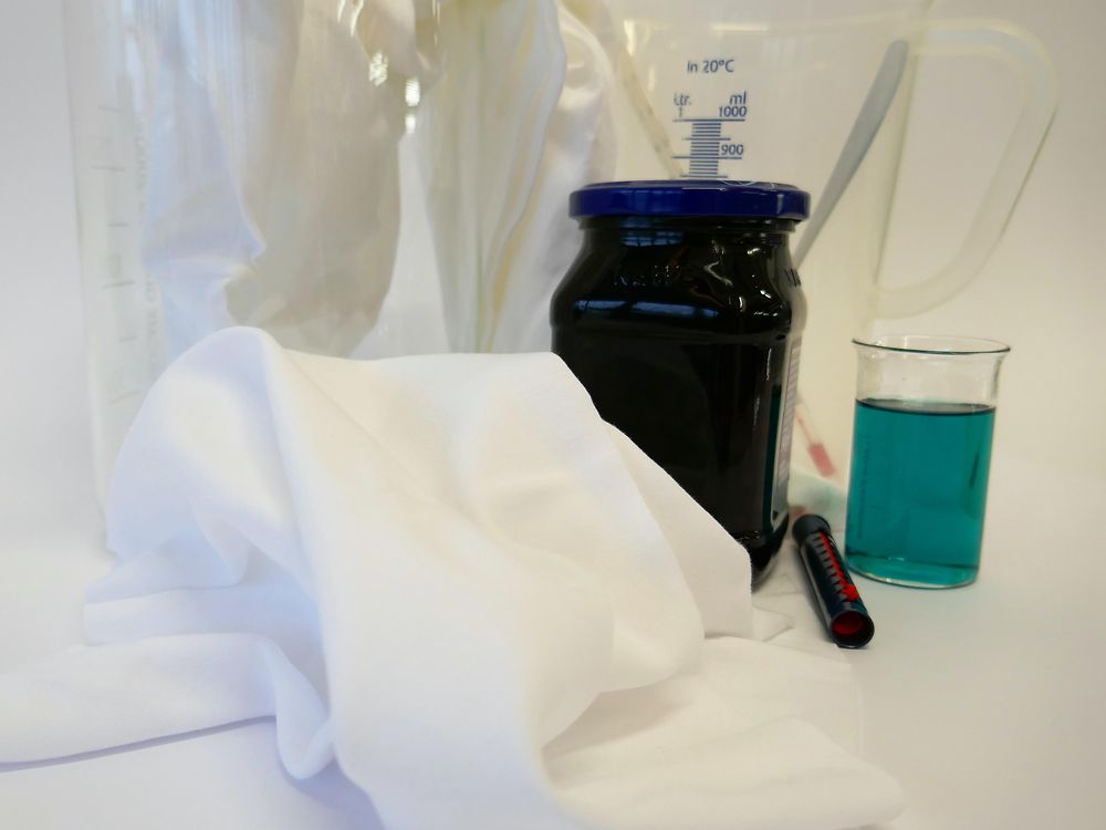 tecido branco, jarro medidor, detergente líquido azul e frasco contendo bagas azuis