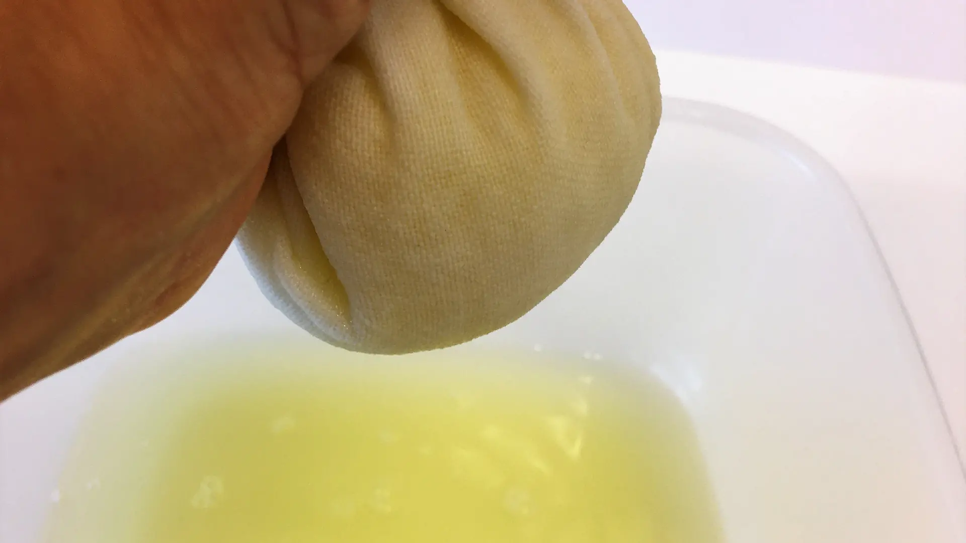 mão espremendo suco amarelo da bola de toalha de chá branca