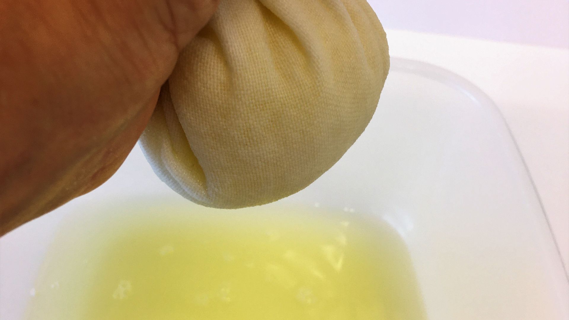 hand squeezing yellow juice from white tea towel ball
