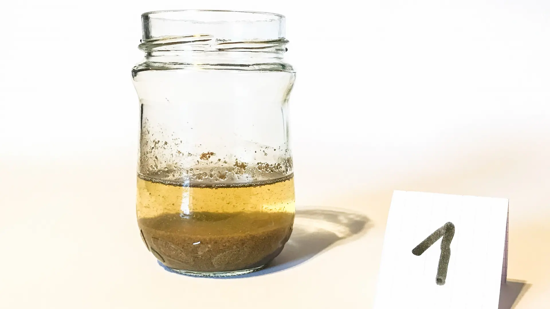glass jar with clear liquid above solid residue