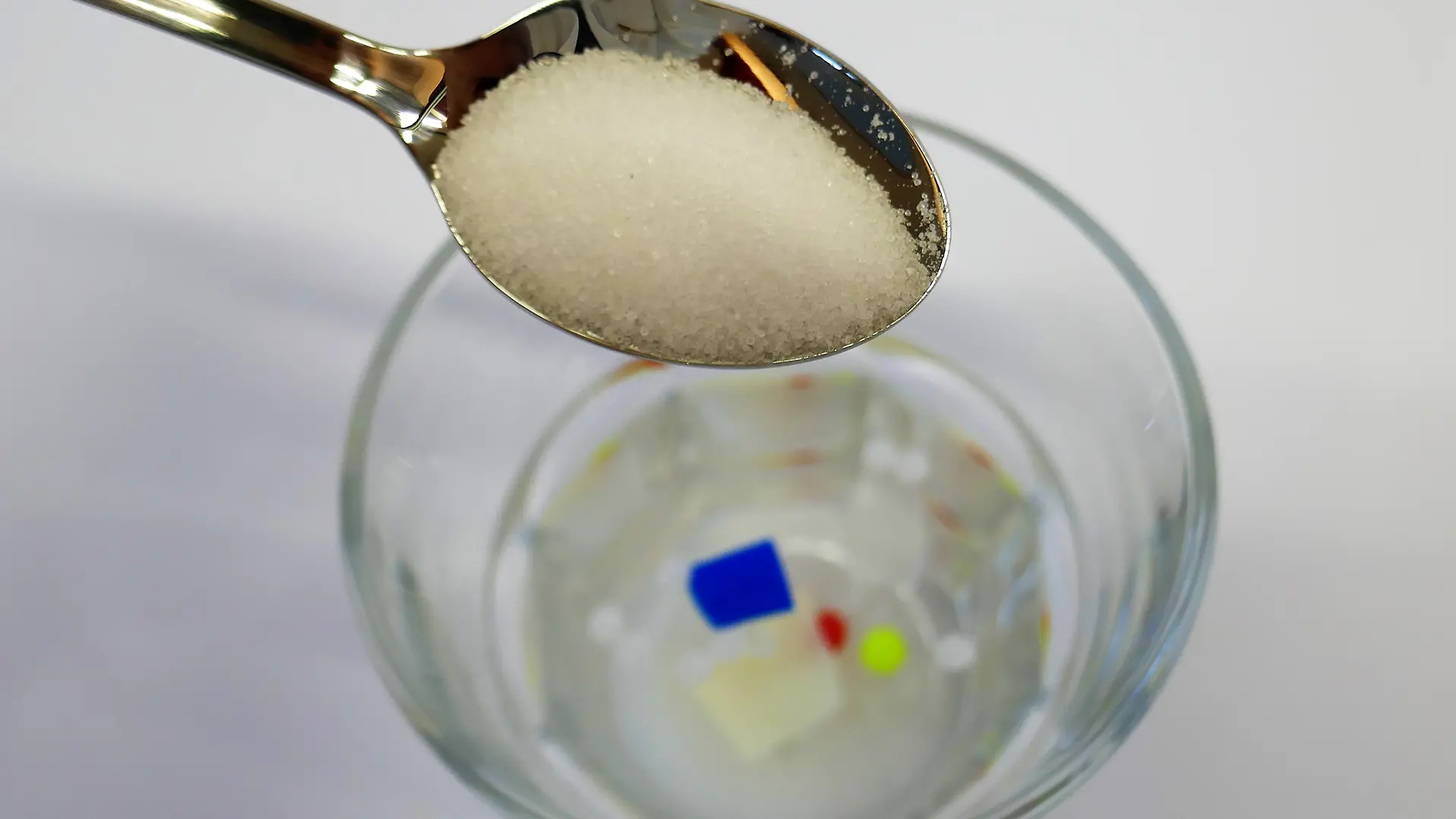 łyżka z solą nad szklanką z pływającymi kawałkami plastiku