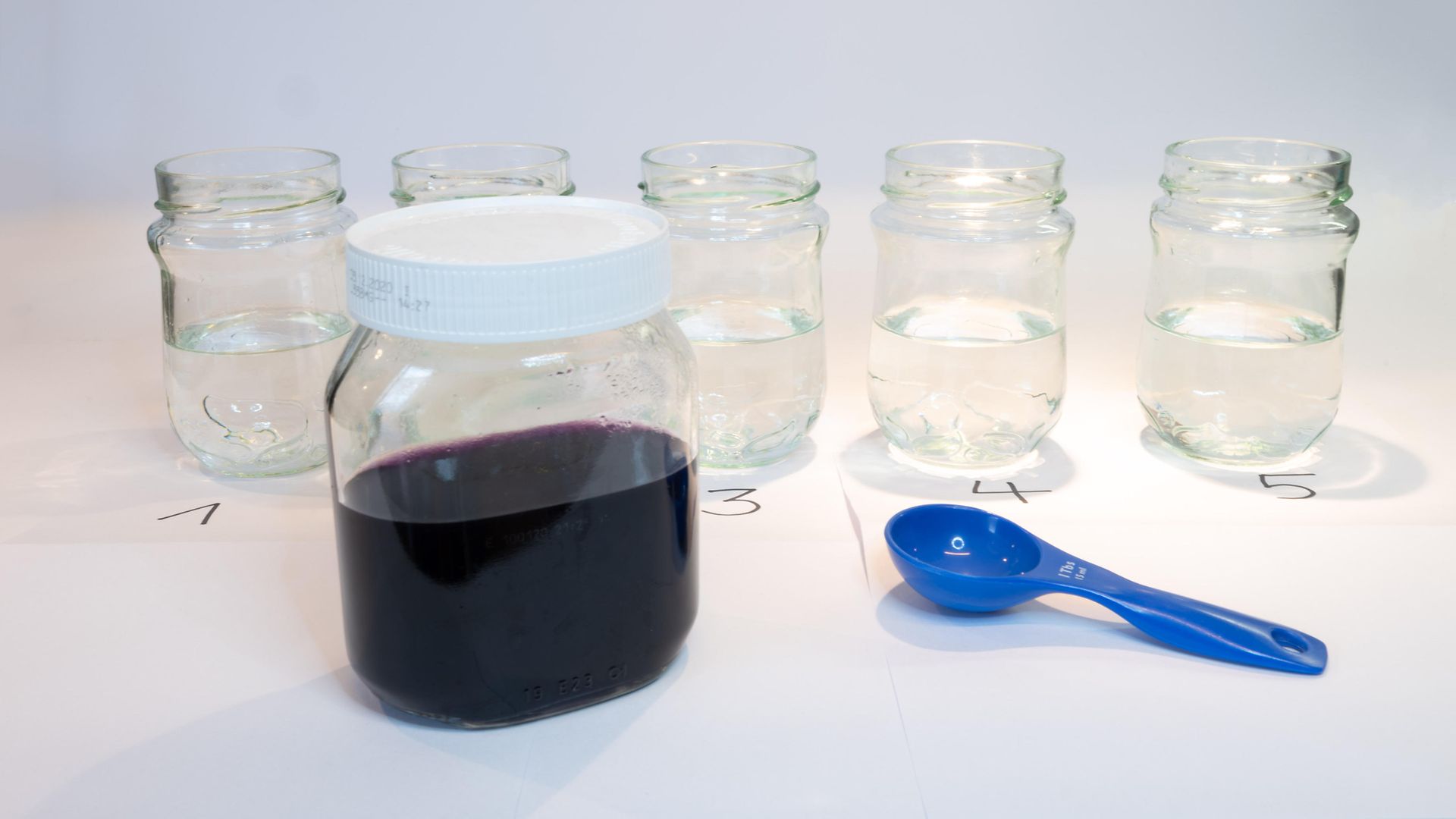 large glass jar with dark liquid in front of five empty glas jars