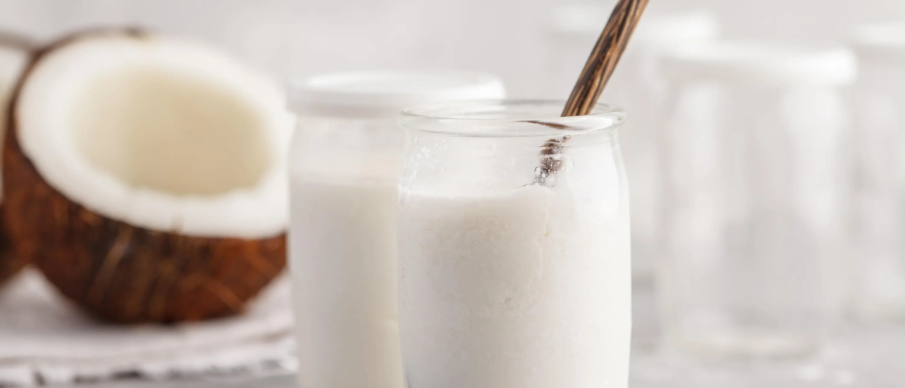 Jogurt-Gläser mit Kokosnusshälfte im Hintergrund