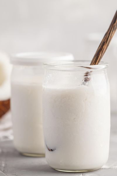 Jogurt-Gläser mit Kokosnusshälfte im Hintergrund