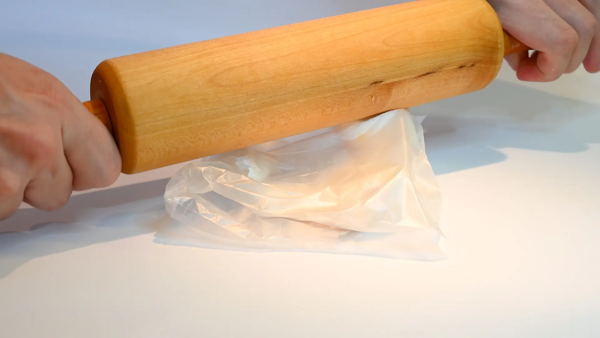 hands with rolling pin which is passed over freezer bag with eggshells