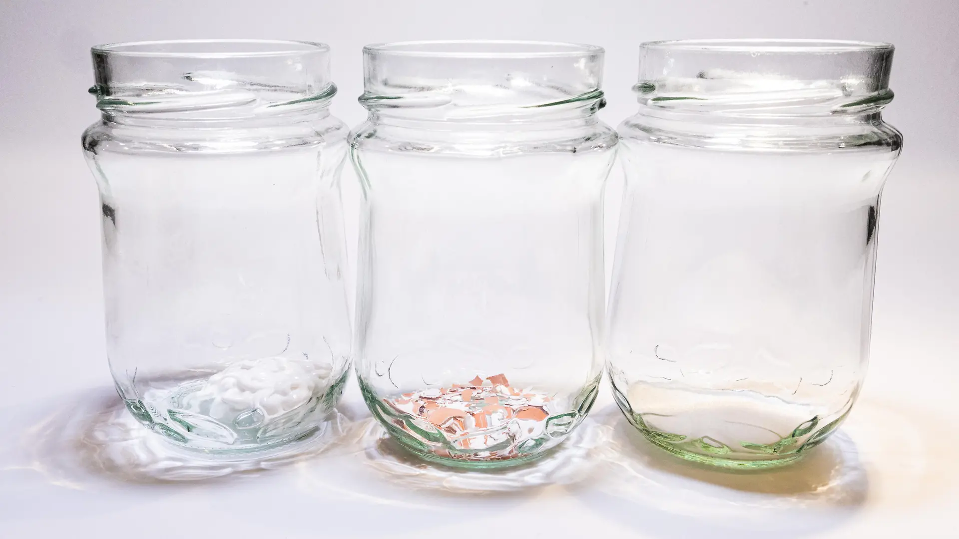 trzy szklane słoiki z płynem, proszkiem ze skorupek i pastą do zębów