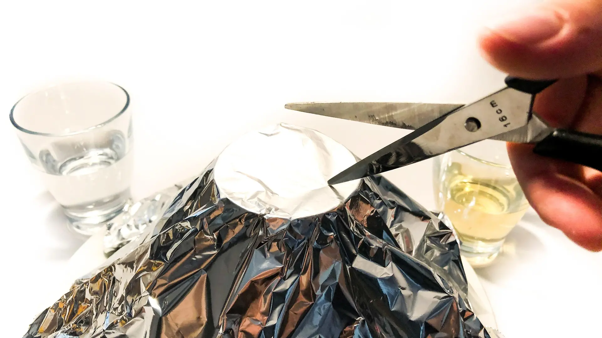 ręka z nożyczkami wycinającymi otwór w stożku folii aluminiowej