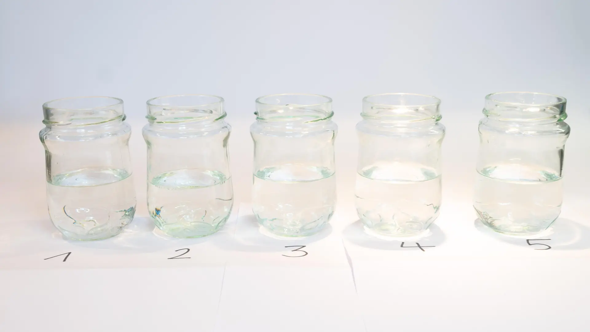 row of five glas jars with clear liquids
