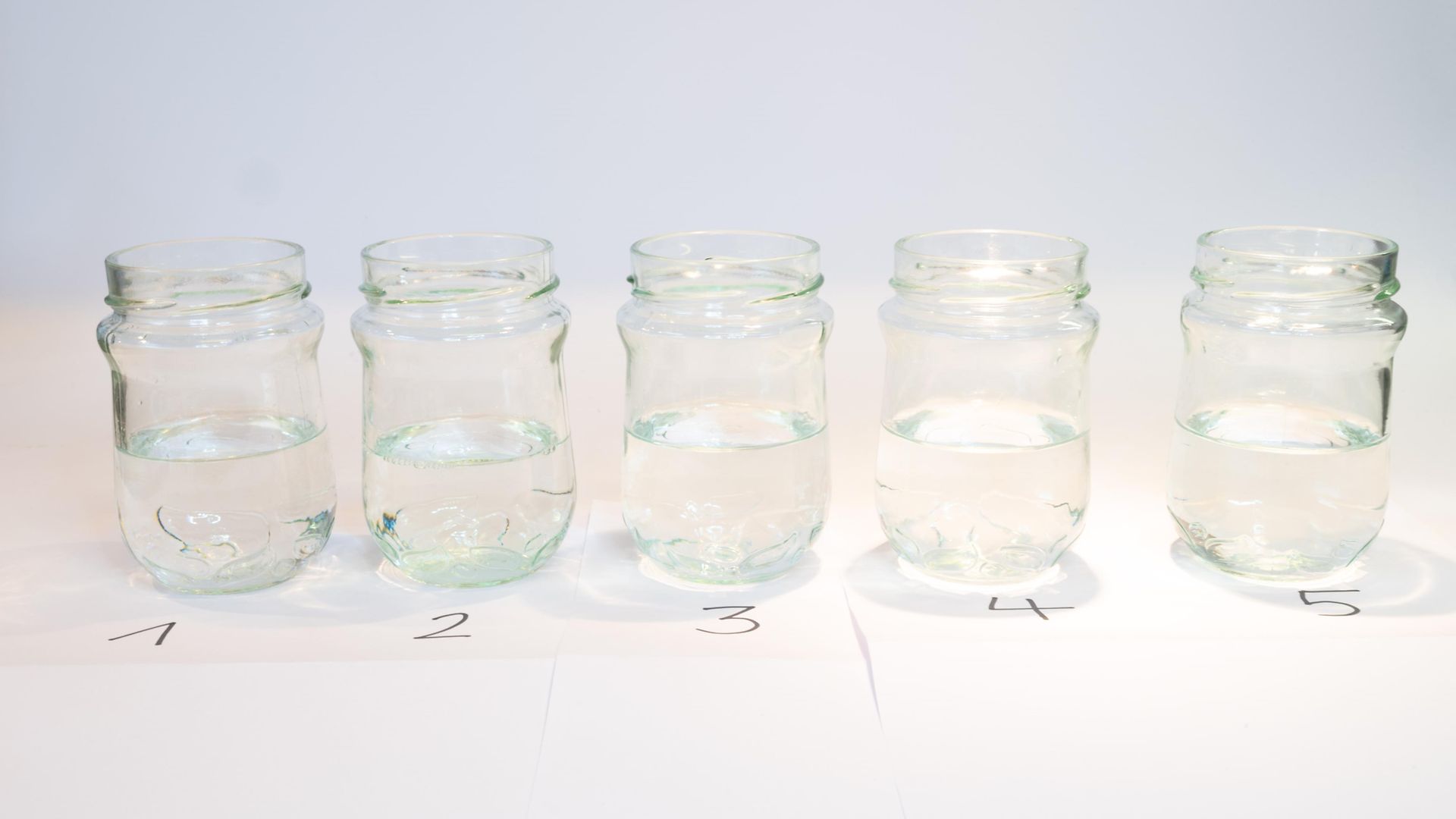 rząd pięciu szklanych słoików z klarownymi płynami