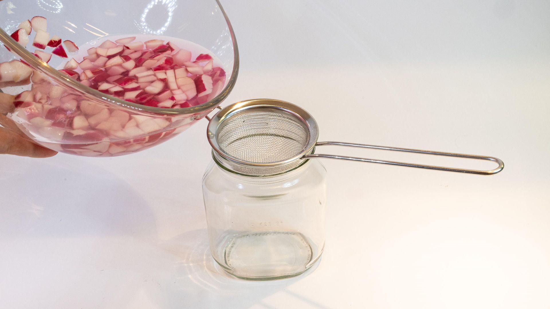 radish juice is poured through sieve into a glass