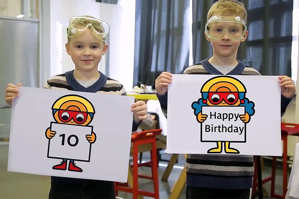 2 blond boys holding paintings with the Text 10 and Forscherwelt