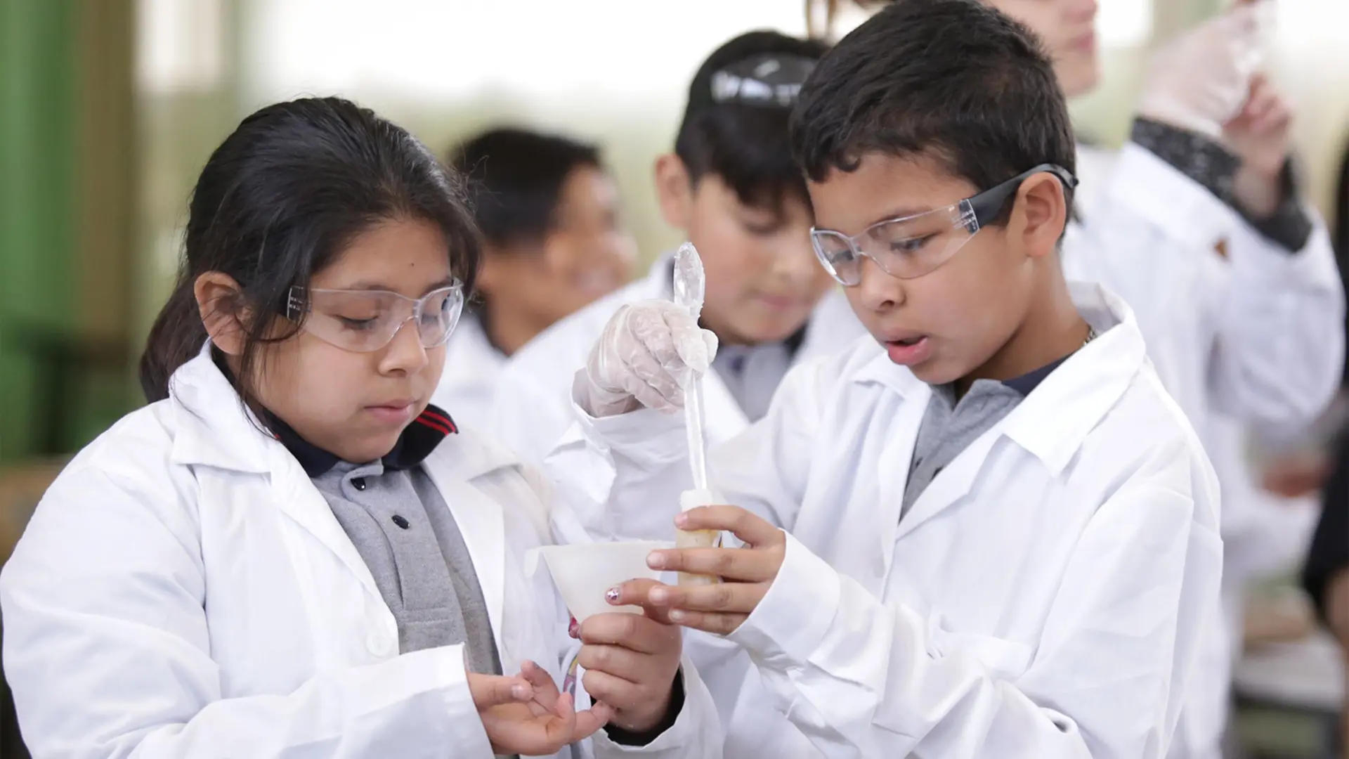 Club Henkel Mundo de Investigadores América Latina: niños con batas de trabajo blancas hacinedo experimentos.