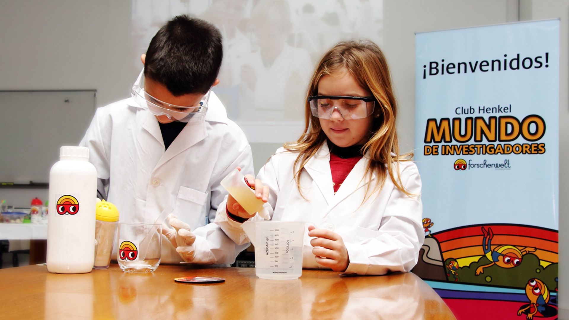 Club Henkel Mundo de Investigadores América Latina: una nina y un niño demonstrando un experiment en una mesa.