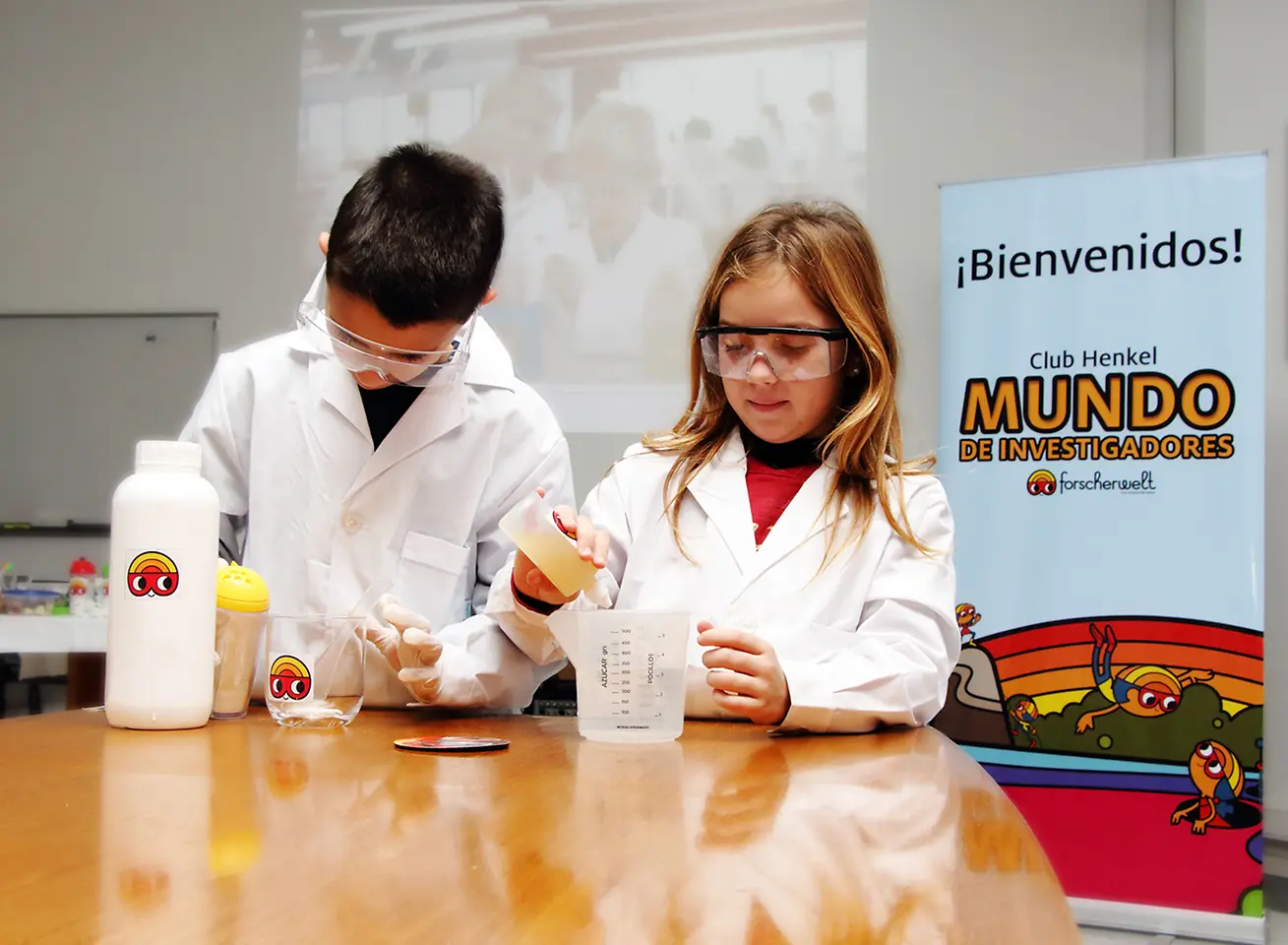 Club Henkel Mundo de Investigadores América Latina: una nina y un niño demonstrando un experiment en una mesa.