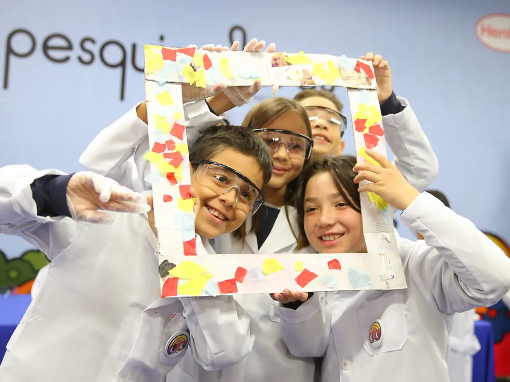 Cuatro estudiantes brasileños miran a través de un marco cuadrado de fabricación propia que hicieron con pegamento de fabricación propia.