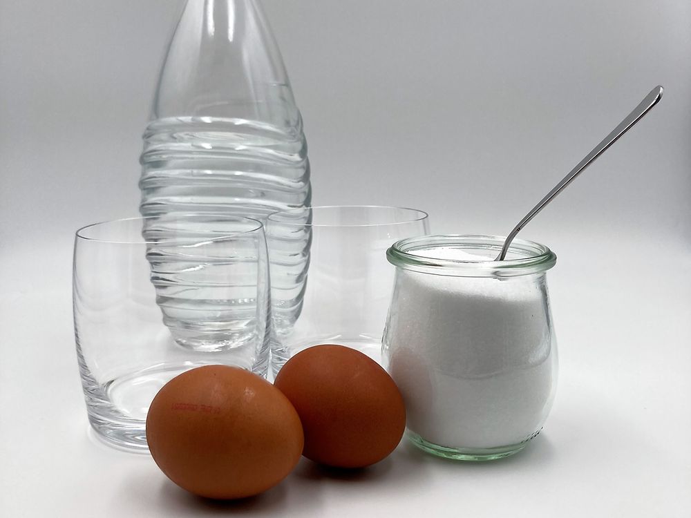 Wasserflasche, zwei Wassergläser, zwei Eier und ein Glas mit Kochsalz und Teelöffel. 