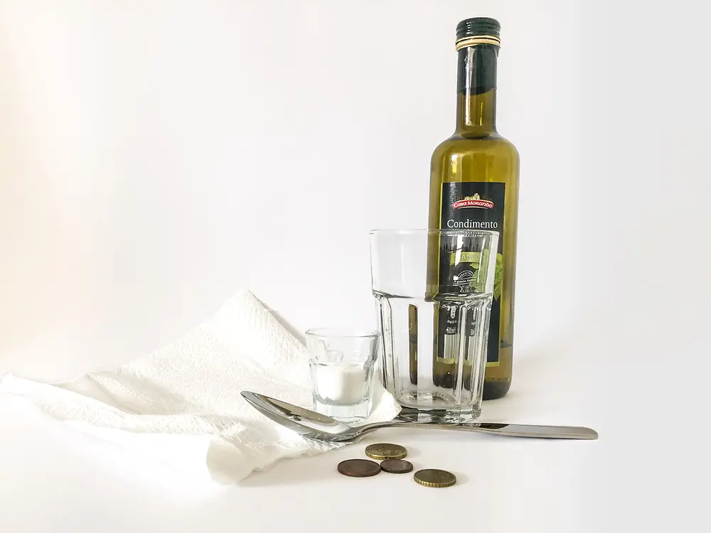 пляшка з оцтом, ганчірка для чищення, склянка, столова ложка, монети та кухонна сіль у баночці