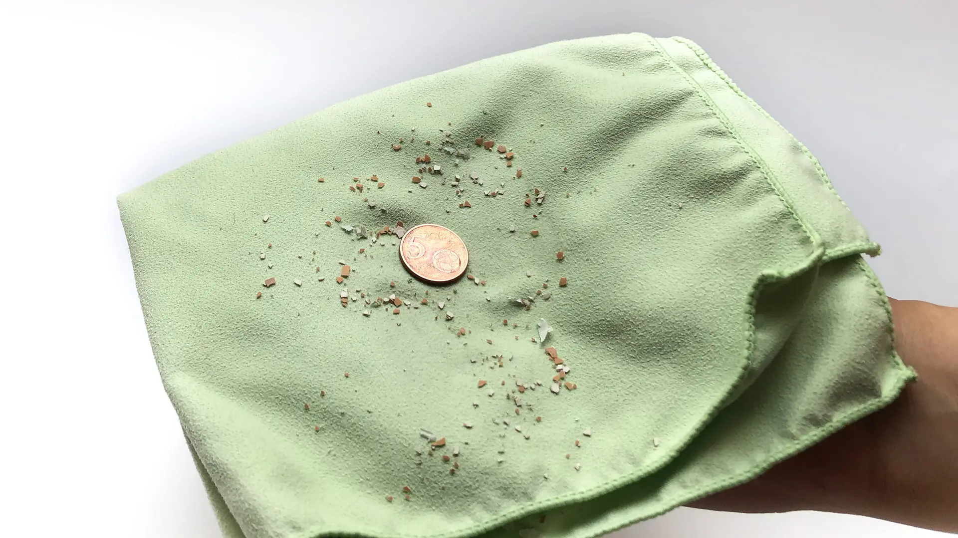 Зелена серветка для чищення з блискучою монетою та порошком з яєчної шкаралупи.