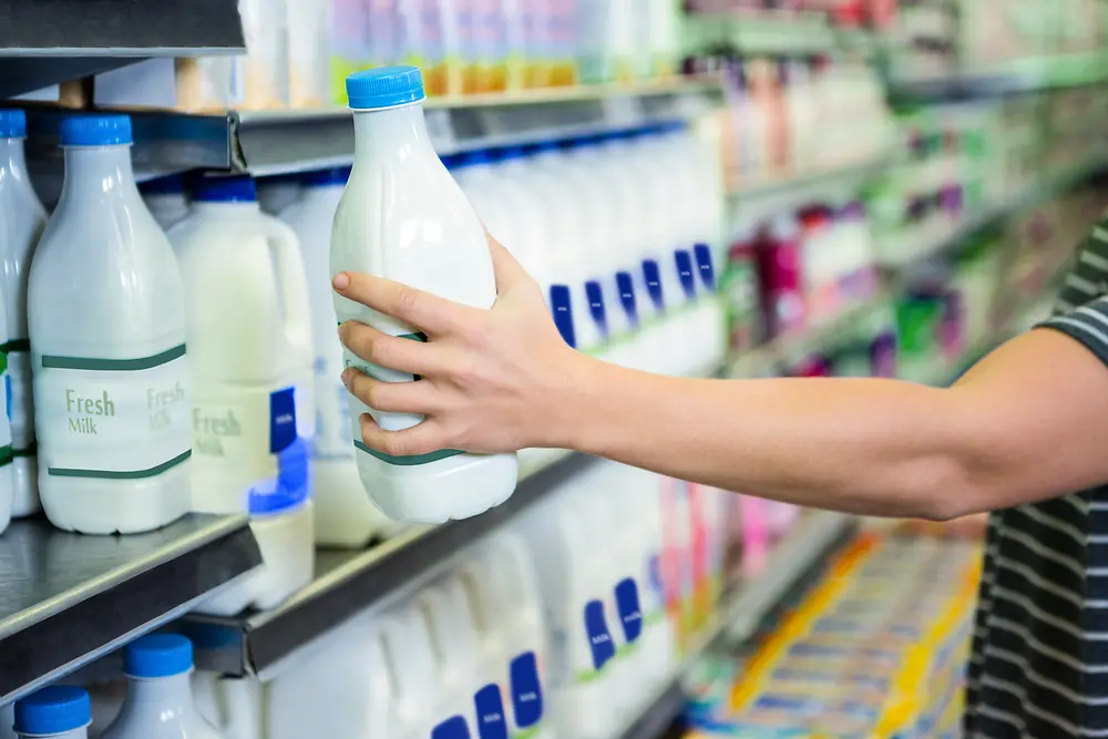 Hand greift nach Milchflasche im Supermarkt-Regal.
