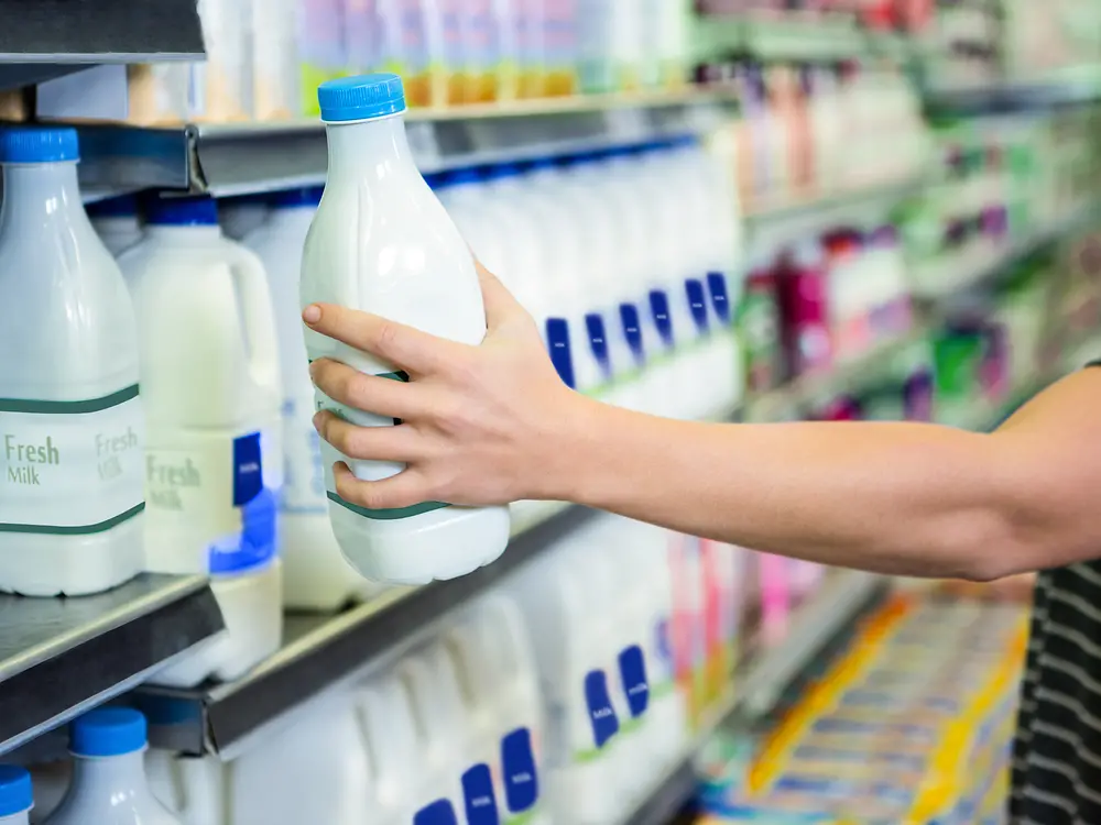 Hand greift nach Milchflasche im Supermarkt-Regal.