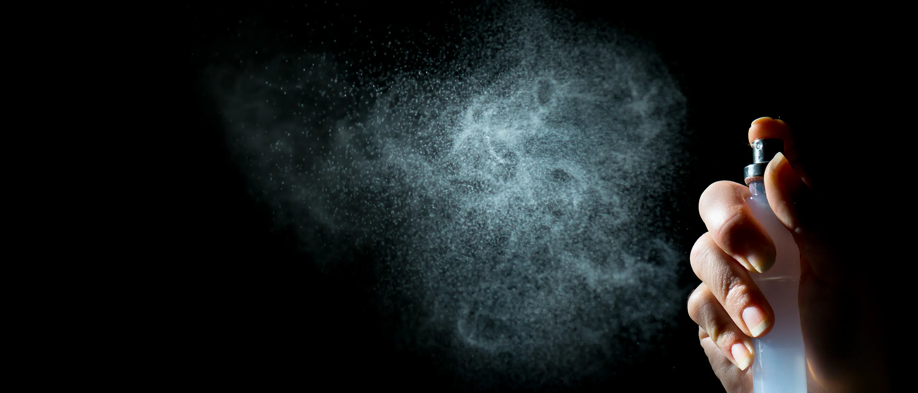 Hand with pump spray, white mist on black background