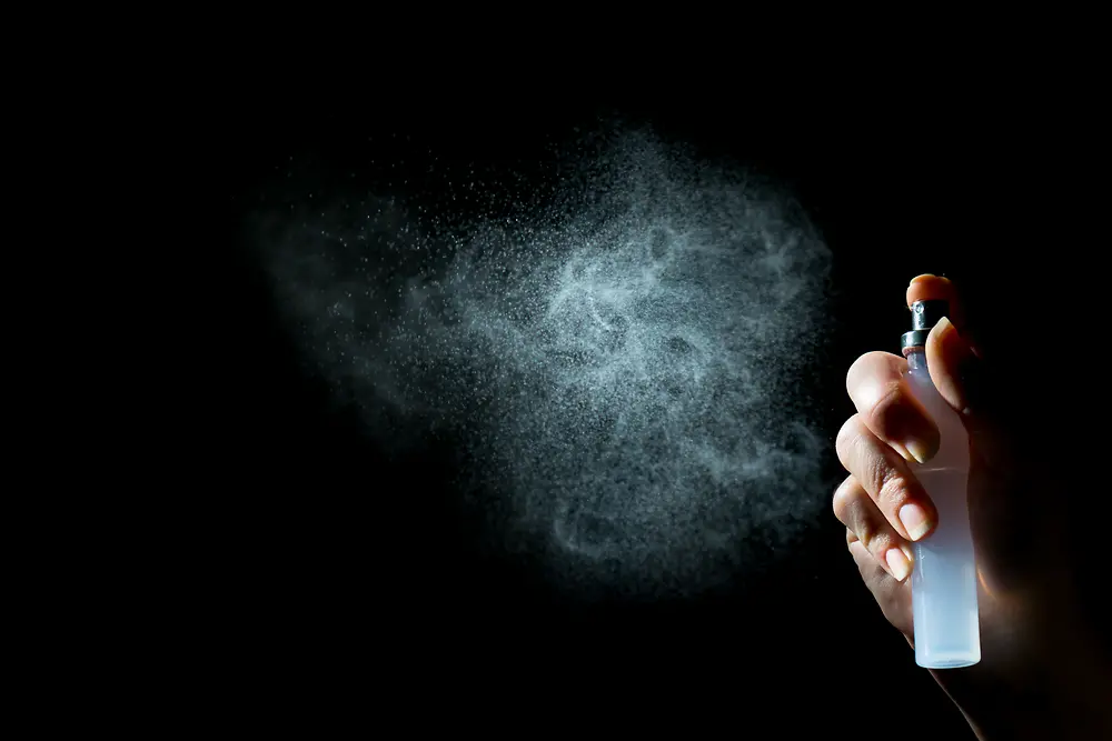 Hand mit Pumpspray, weißem Nebel vor schwarzem Hintergrund