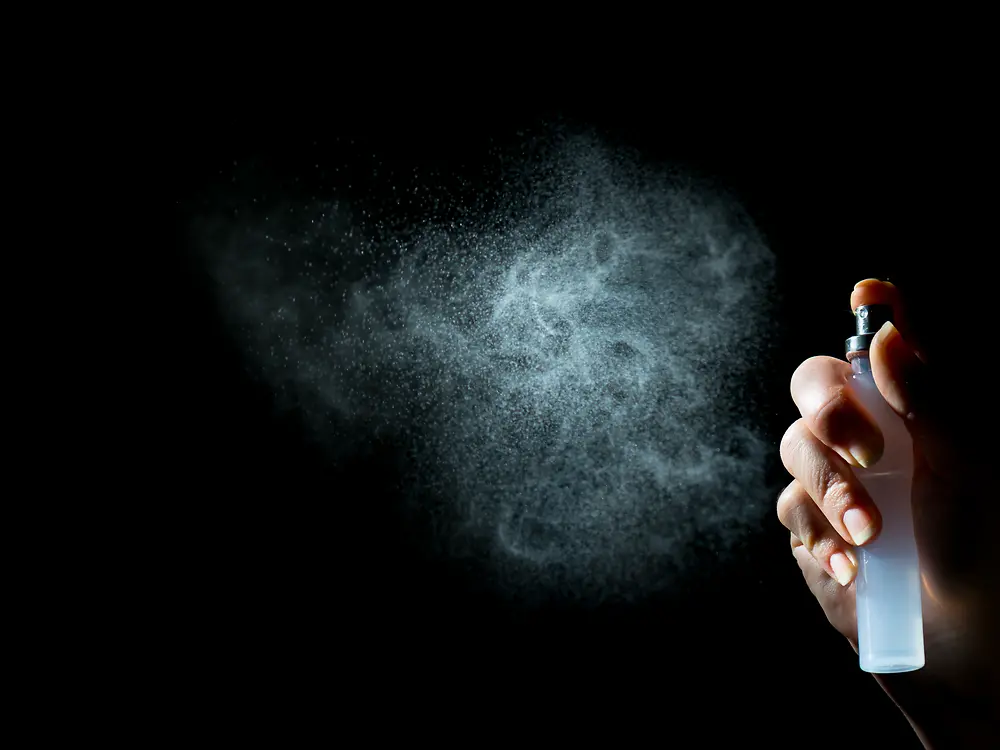 Hand mit Pumpspray, weißem Nebel vor schwarzem Hintergrund