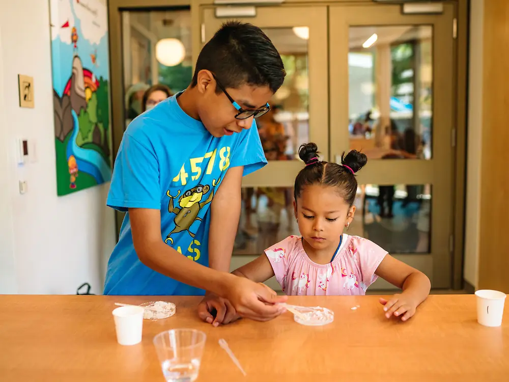 Volunteer aids student in mixing a paste for energy experiment.
