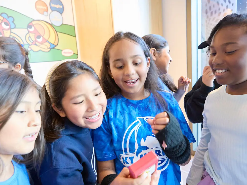 Students smiling excitedly while observing a device in action.