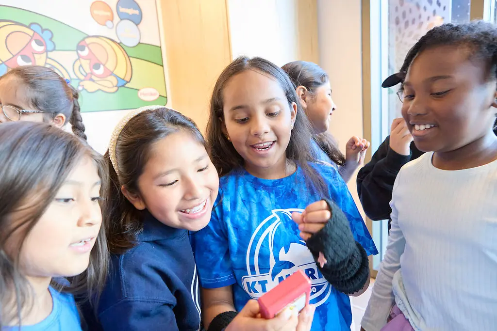 Students smiling excitedly while observing a device in action.