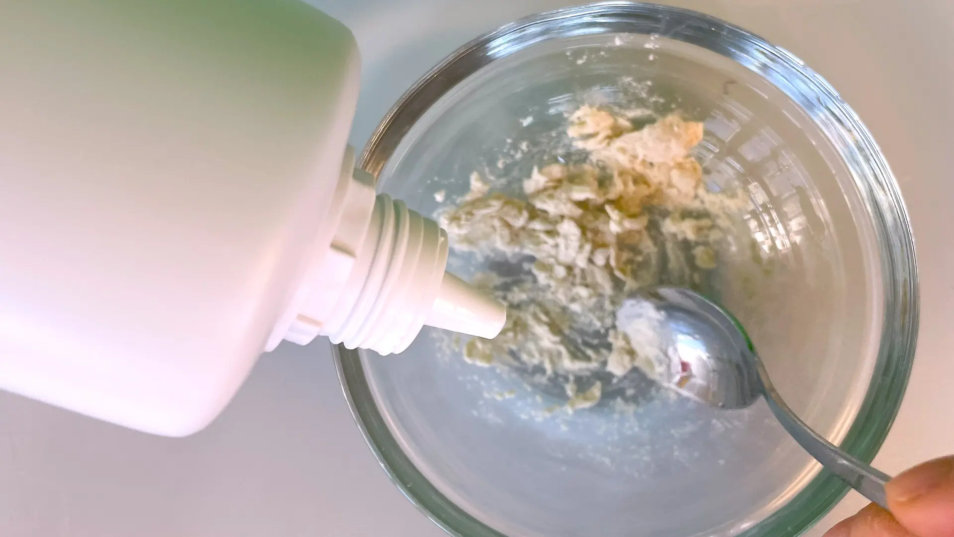 Mit einem kleinen Löffel wird etwas Guarkernmehl zusammen mit ein wenig Kontaktlinsenflüssigkeit in einer Glasschüssel verrührt.